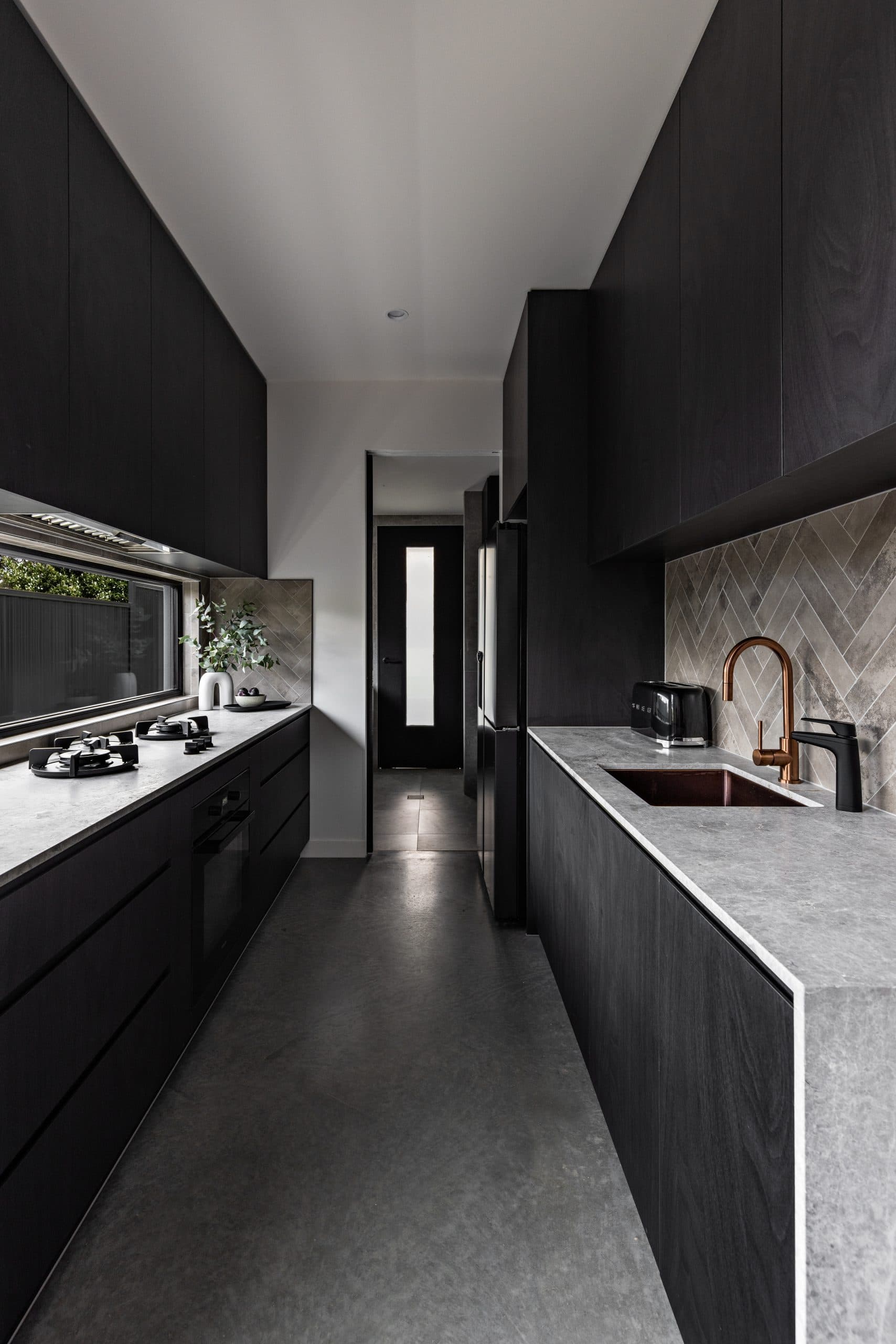 Sleek modern galley kitchen featuring dark cabinetry, grey stone countertops, and a copper sink faucet.