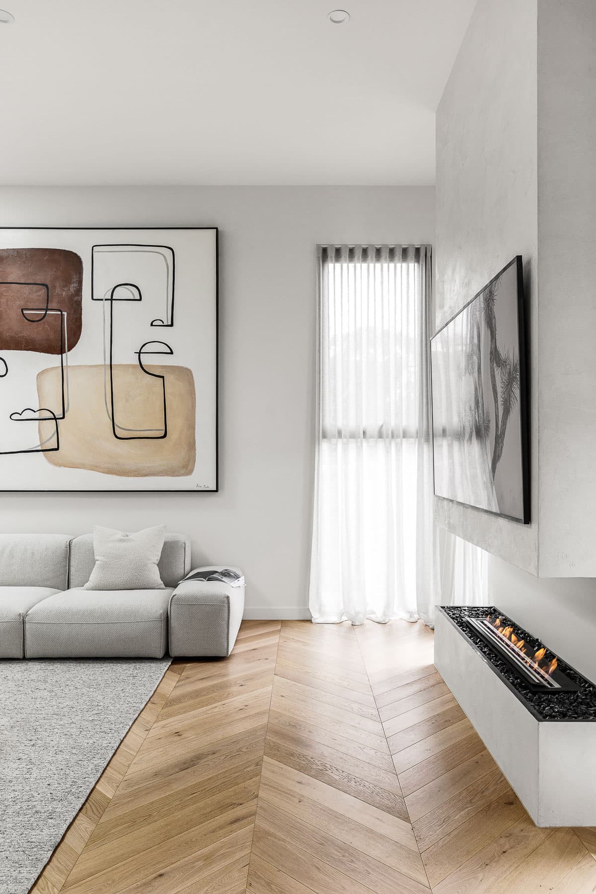 Modern living room featuring abstract art, gray sofa, chevron wood floors, and a linear fireplace.